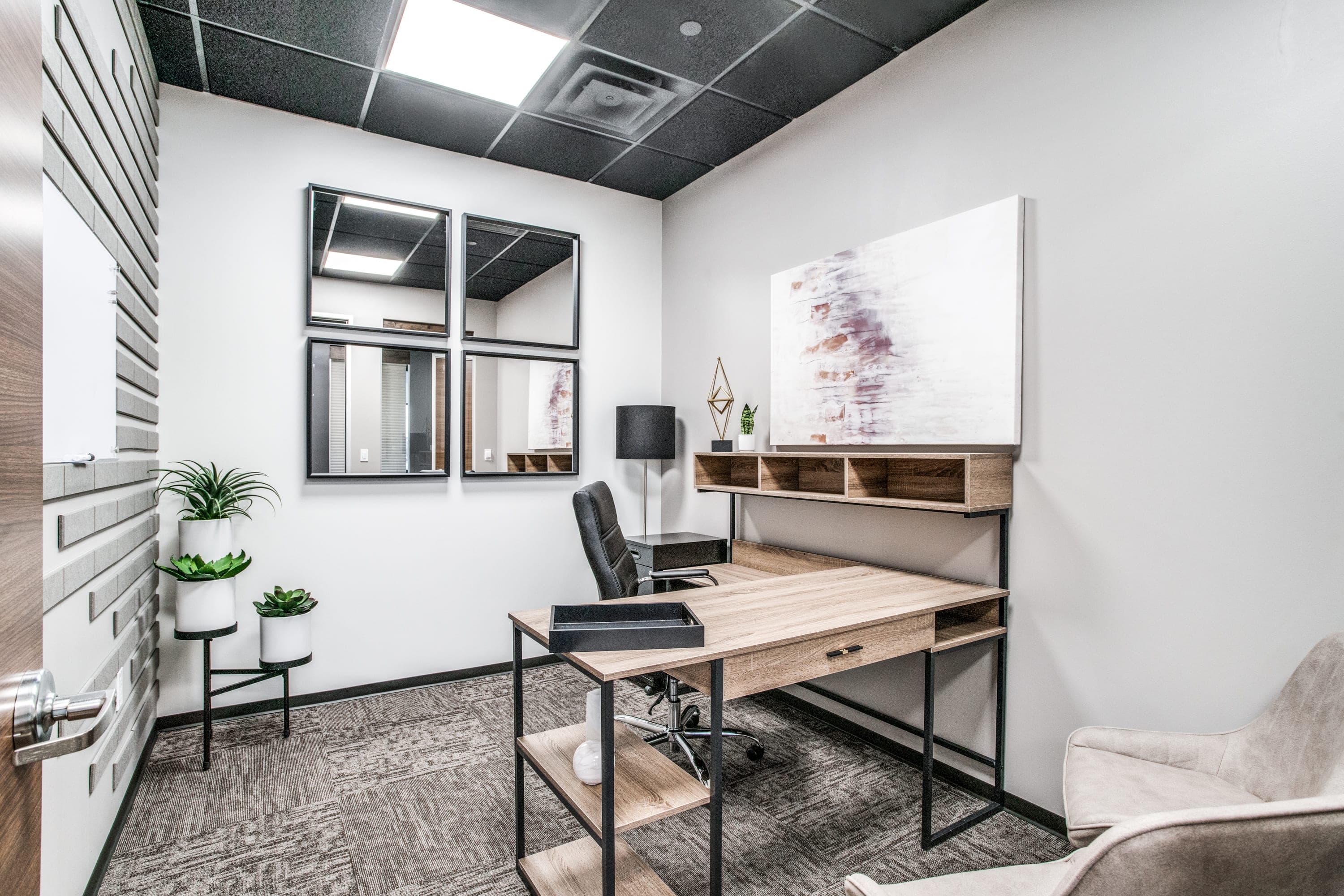 Interior private office with an L-shaped desk, mirror decor, artwork on the walls, and plants in the corner