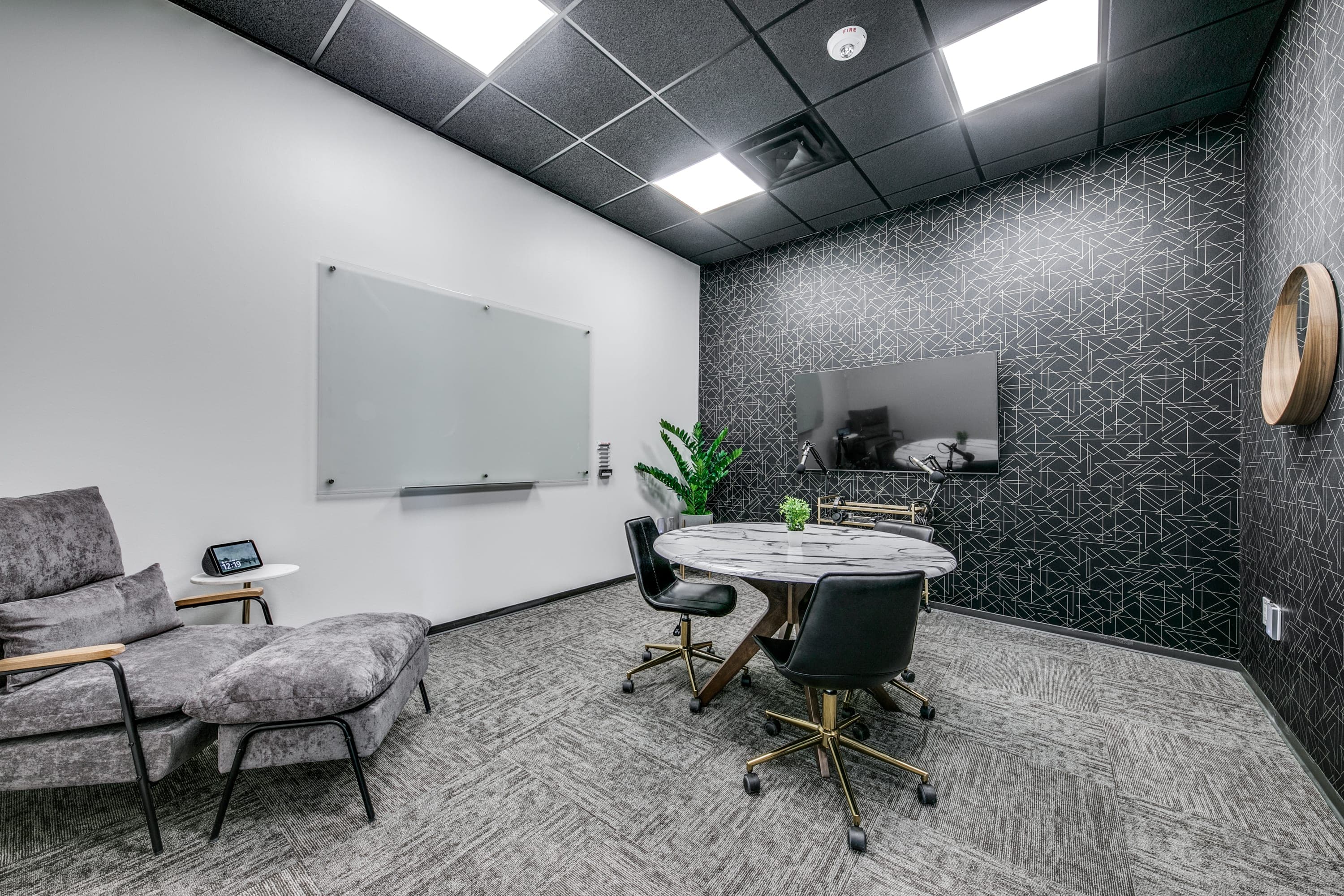 Small meeting room with podcast equipment, a glass dry-erase board, a small table with three seats, a guest chair, and modern decor