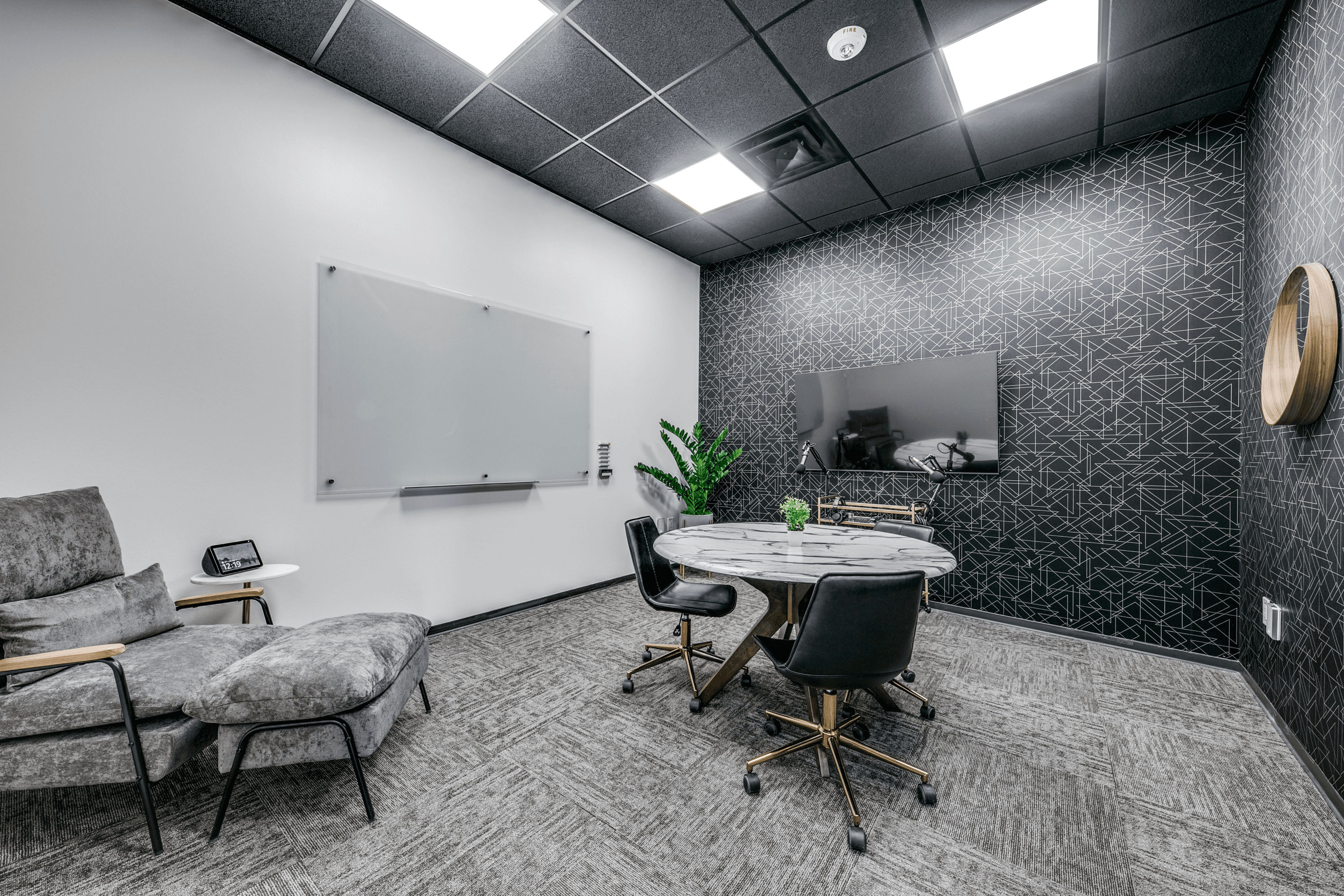 Small meeting room with podcast equipment, a glass dry-erase board, a small table with three seats, a guest chair, and modern decor