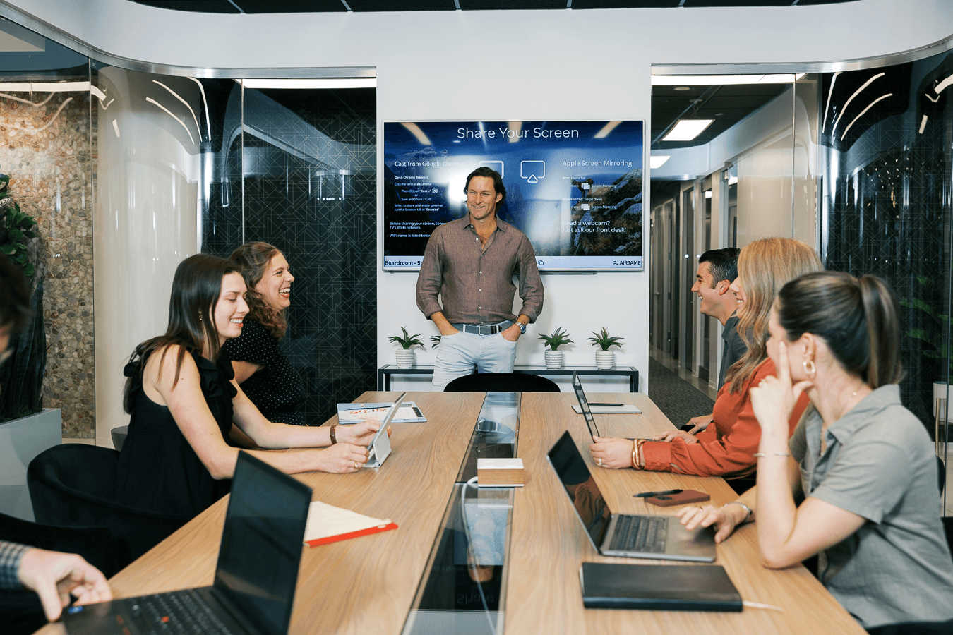 A full meeting room with a presenter and colleagues in front of a TV with screenshare technology